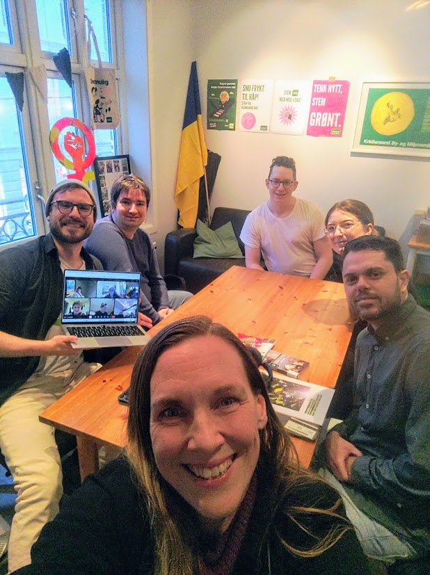 Fem studenter rundt et bord og en voksen gjest i forgrunnen (som har tatt bildet)